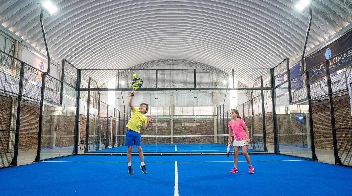 Dos niños jugando un punto de pádel en pareja en la cancha indoor de Padel Lomas