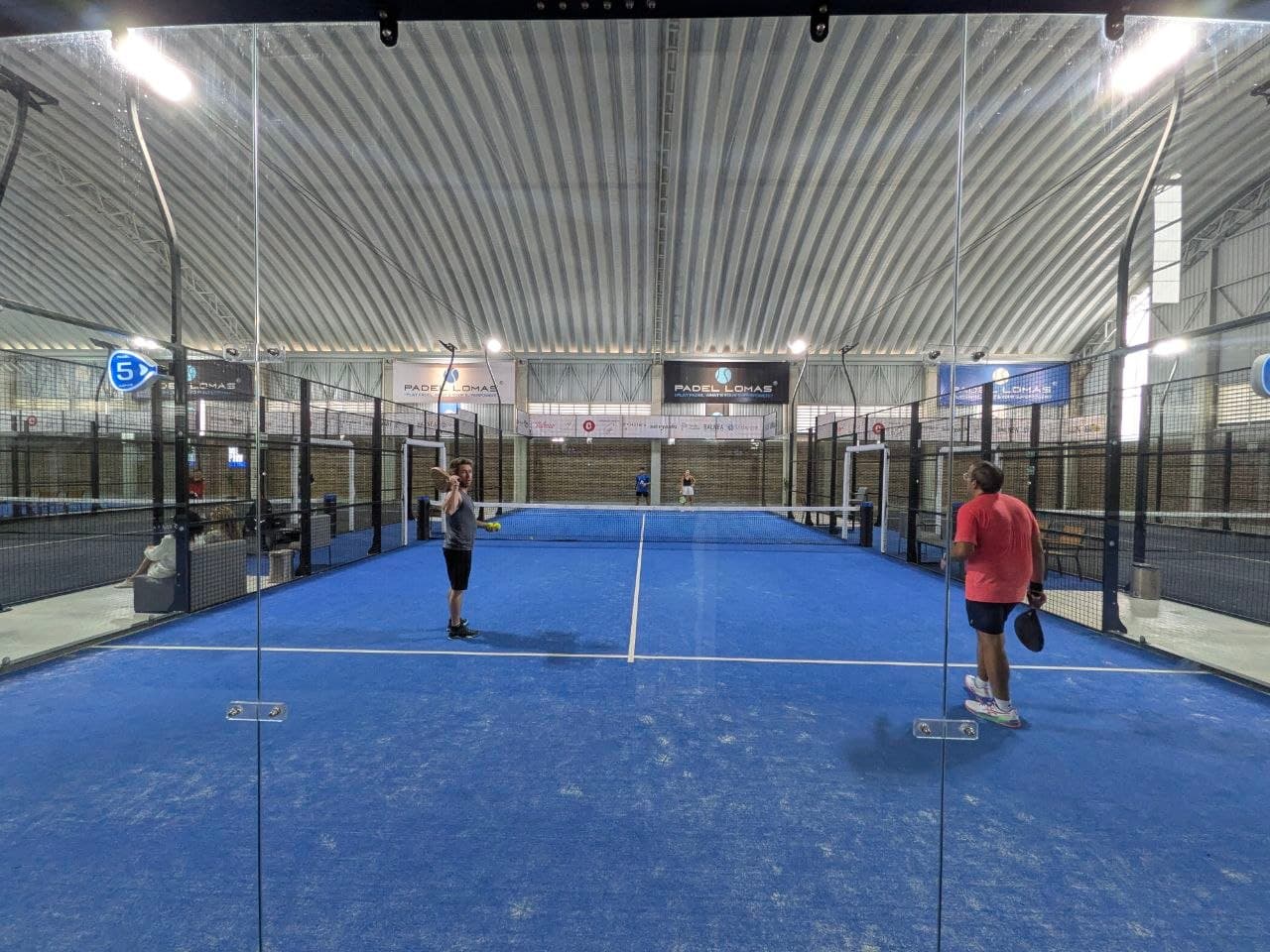 Dos jugadores en plena reta vistos a través del cristal de la cancha azul