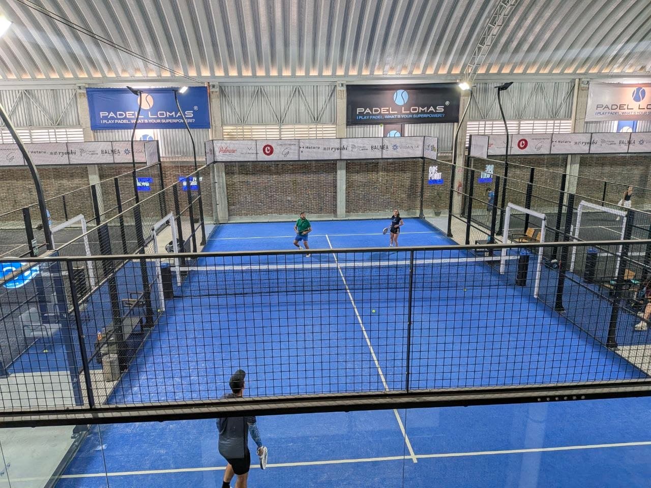 Vista elevada de un partido de pádel en Padel Lomas con jugadores en dos canchas y lonas del club