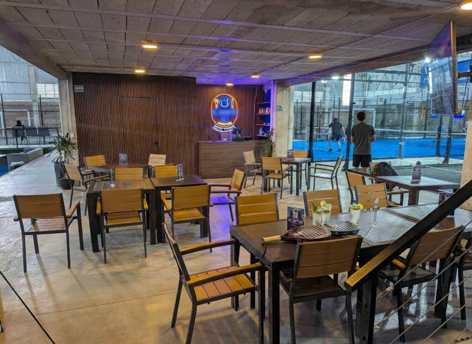 Ambiente después del partido en "El Quinto Set": palas y bebidas en la mesa con la cancha azul al fondo